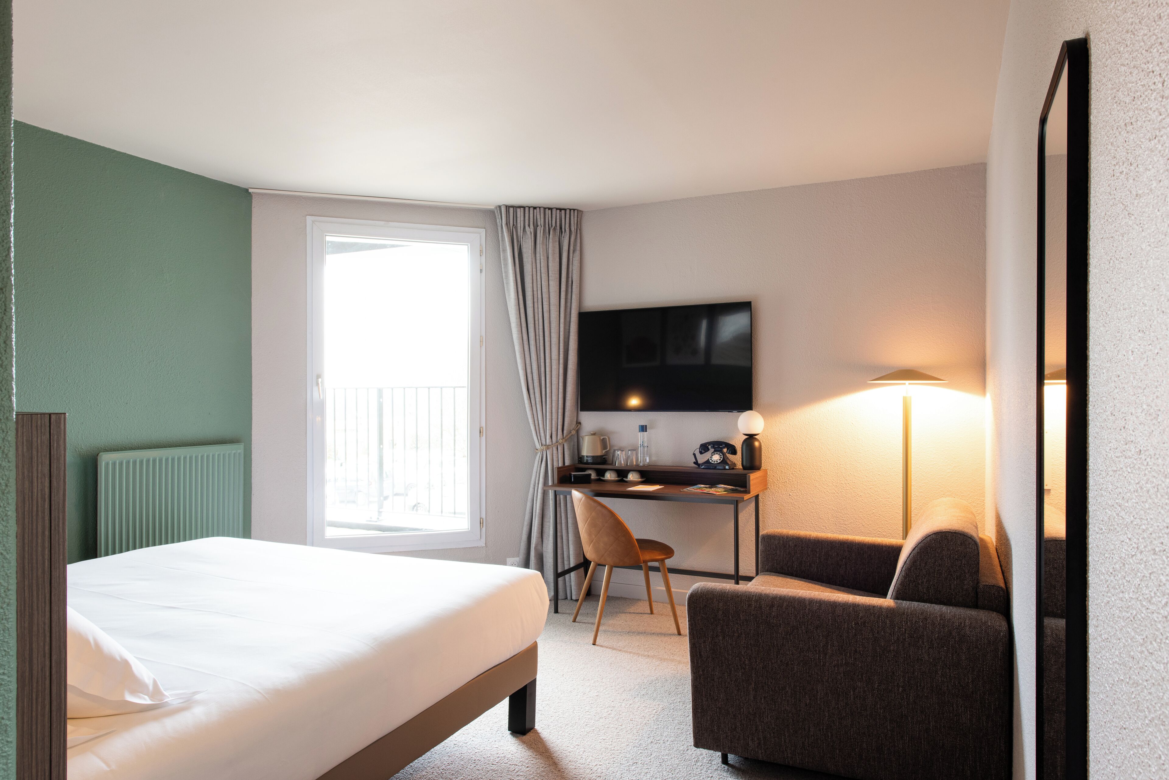 Una habitación de hotel con una cama, un escritorio, una silla, un televisor y una lámpara.