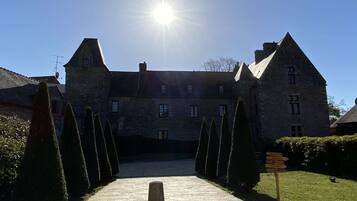 A large stone building with a symmetrical facade, a central entrance, and a well-maintained lawn with trimmed hedges.