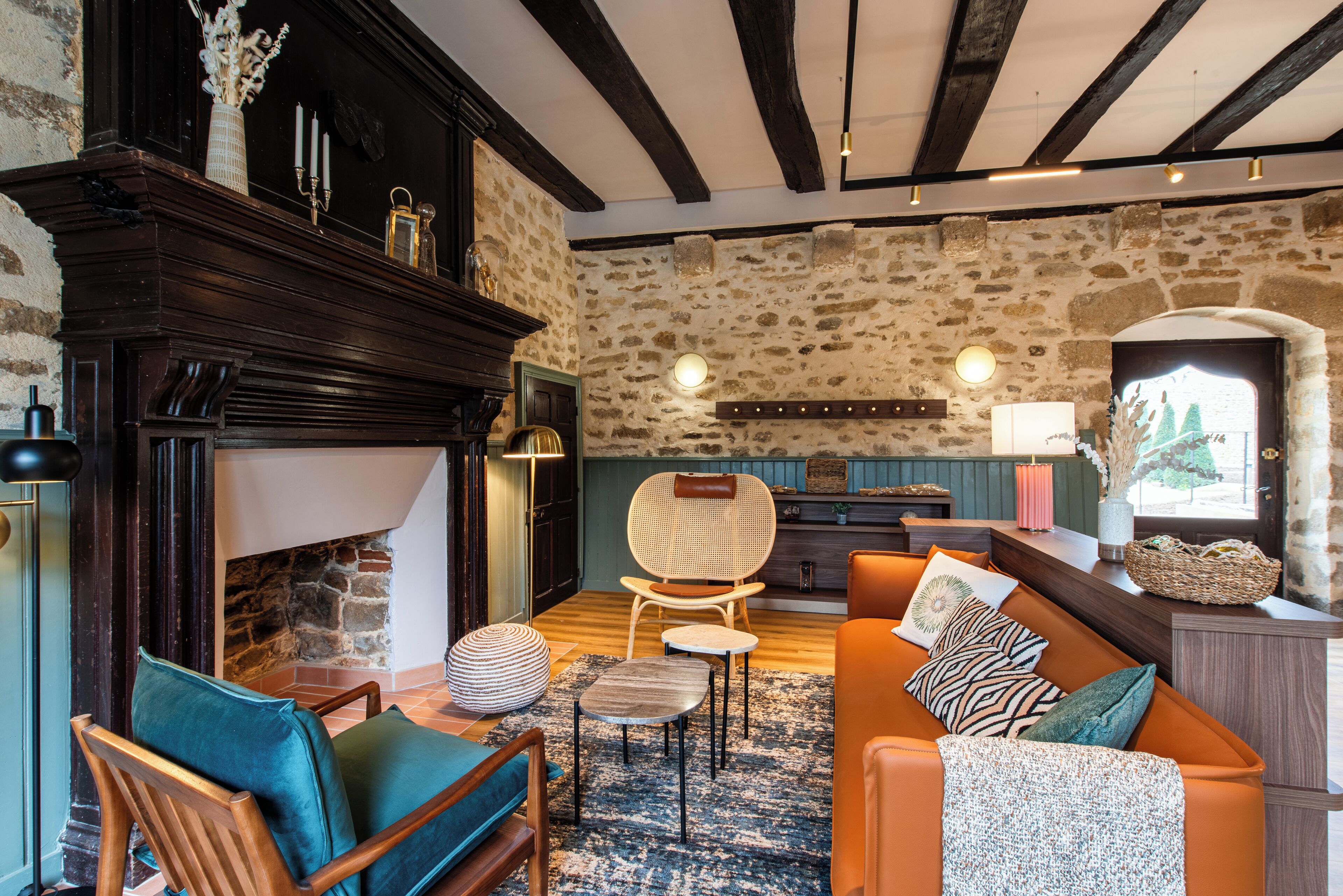 Un salon chaleureux avec une cheminée, des murs en pierre, des poutres en bois et un mélange de meubles modernes et classiques.