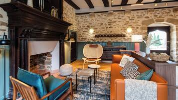 Un salon chaleureux avec une cheminée, des murs en pierre, des poutres en bois et un mélange de meubles modernes et classiques.