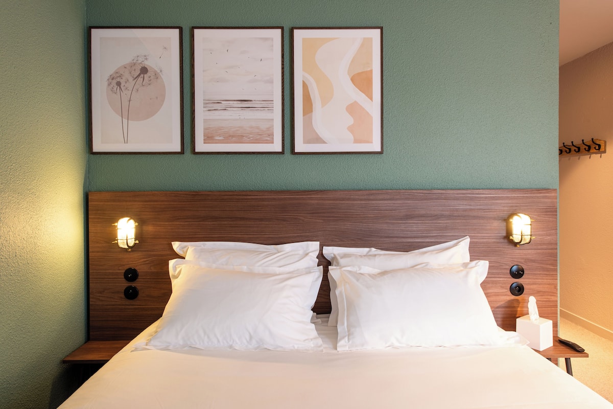 A neatly made bed with white linens, a wooden headboard, and wall-mounted light fixtures.
