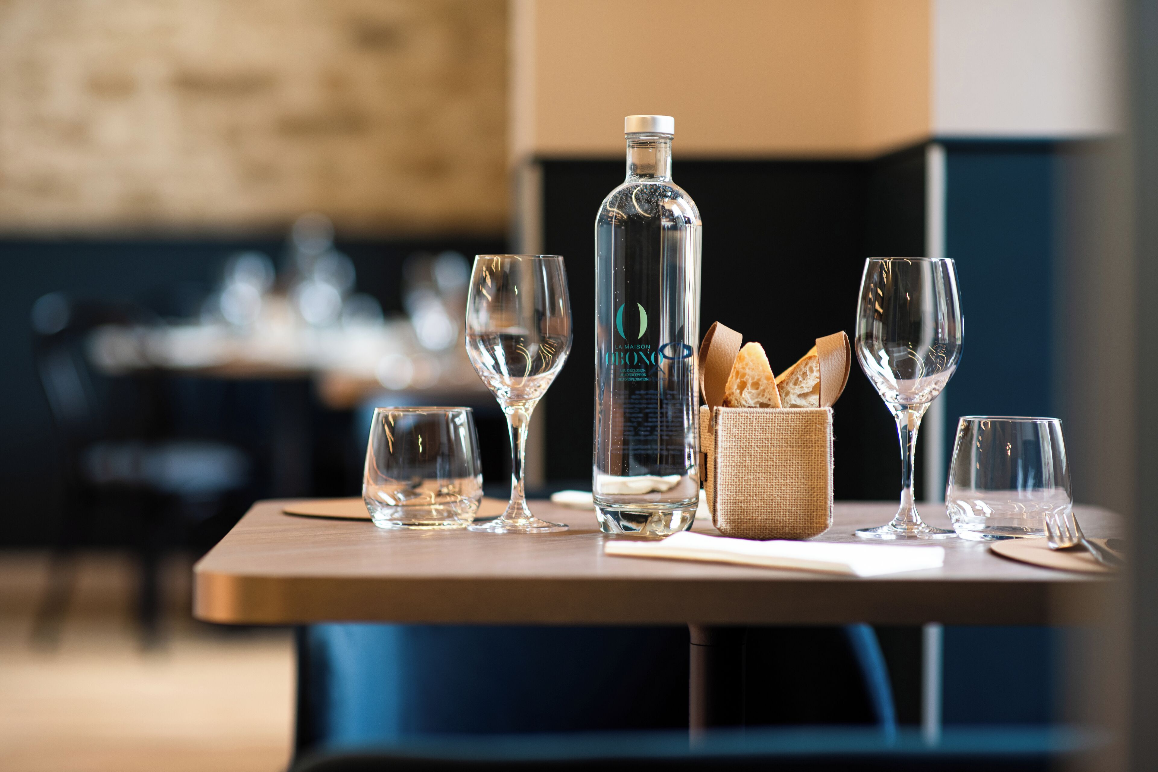 Una mesa con una botella, vasos y una cesta de pan.