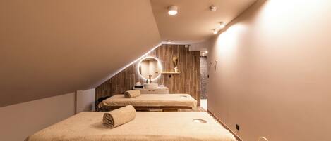 A spa room with two massage tables, a vanity with a mirror, and a decorative lantern.