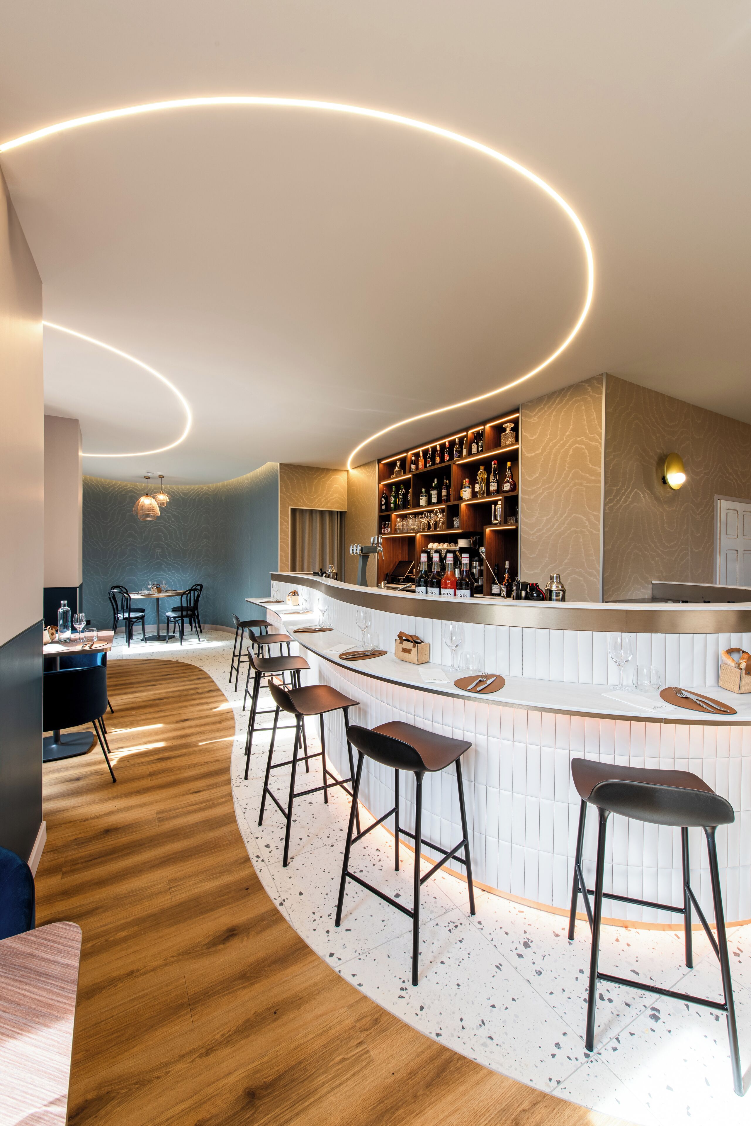 Un área de bar moderna con una barra curva, taburetes y una estantería para vinos.