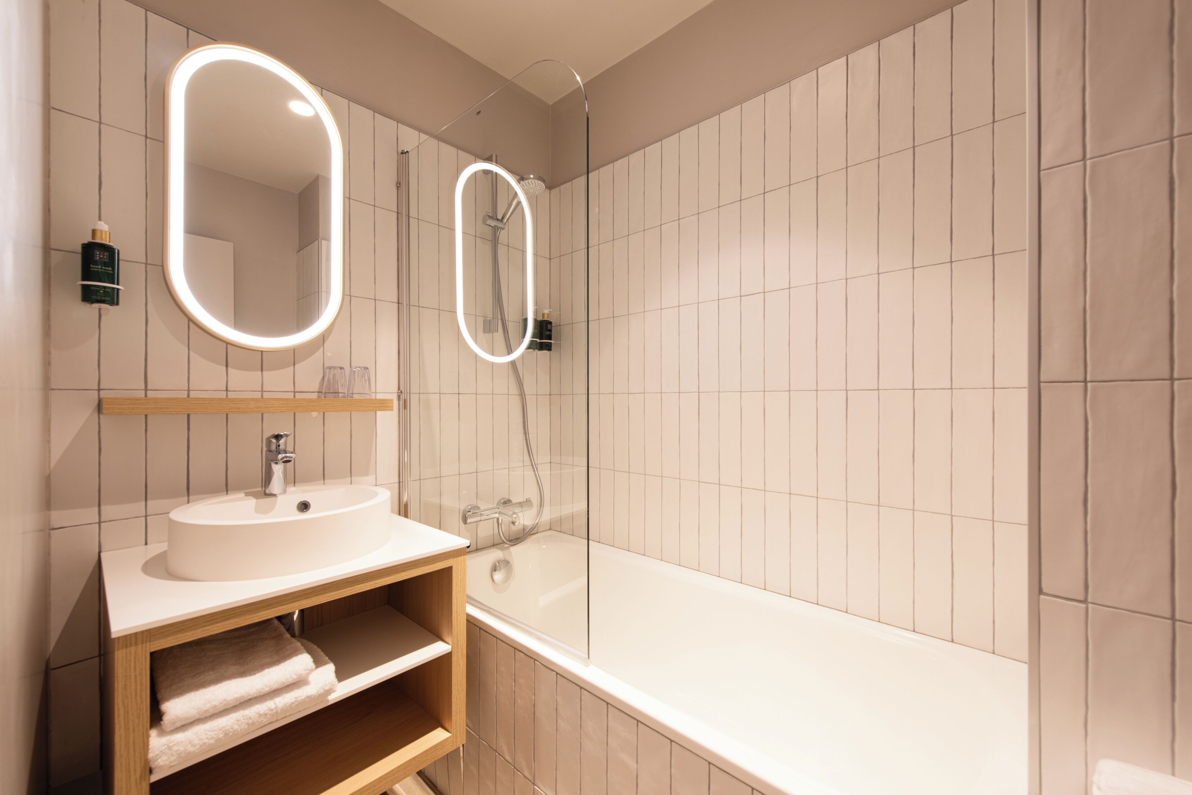 Et moderne badeværelse med en hvid vask, et spejl med oplyst ramme, en bruseniche og et badekar.