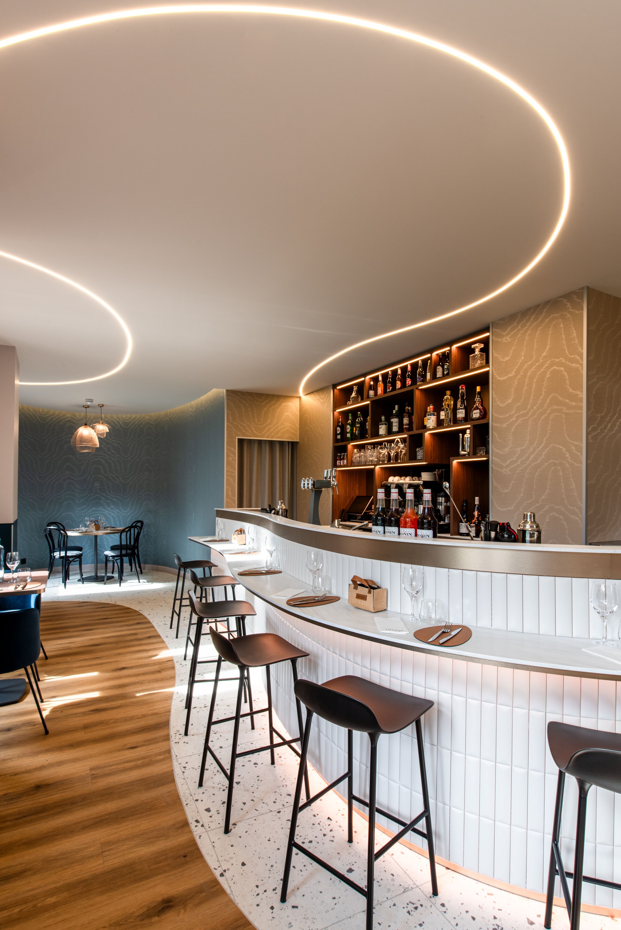 A modern bar area with a curved counter, bar stools, and a wine rack.