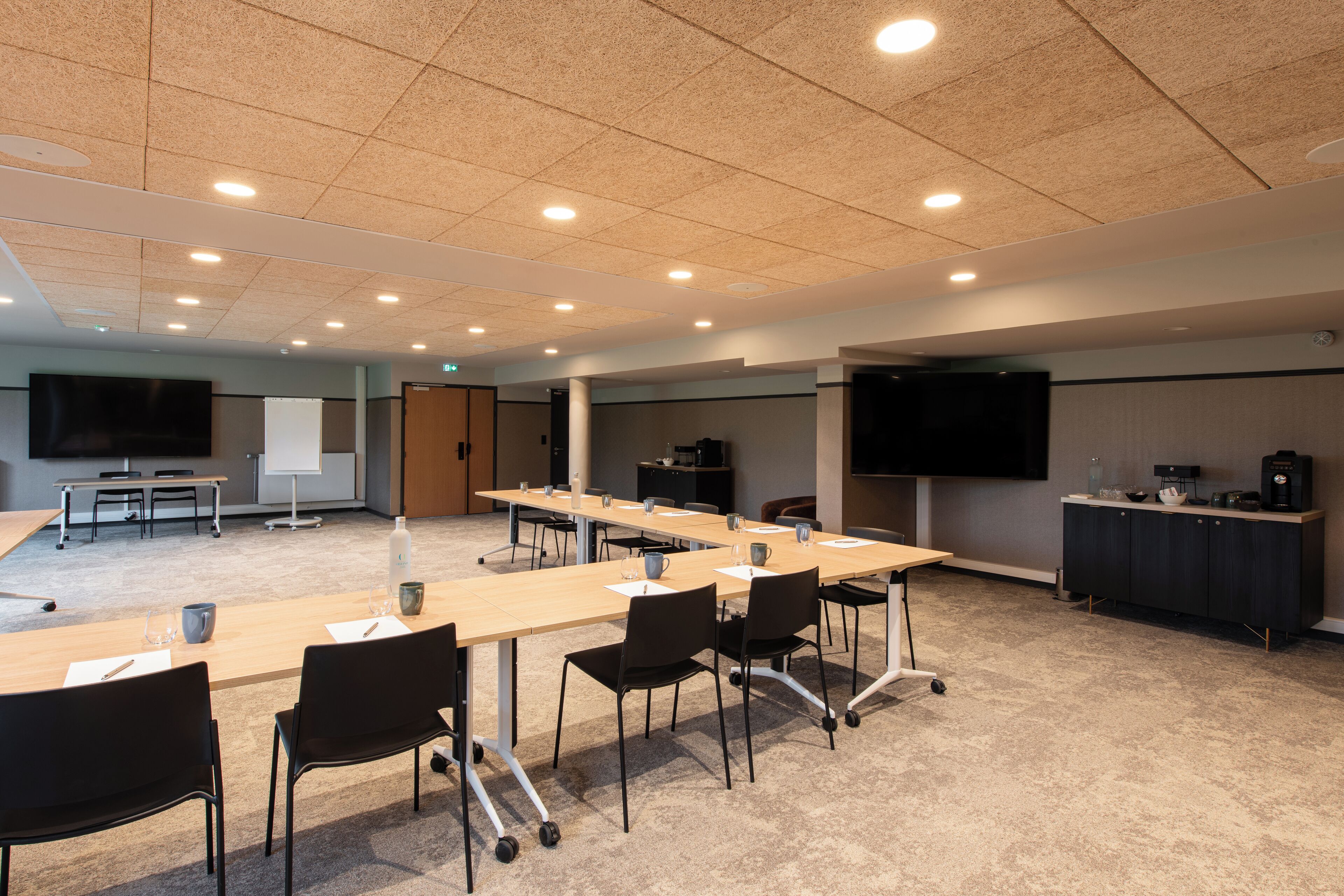 Un salón de conferencias con una larga mesa, sillas, una pantalla de proyector y una estación de café.