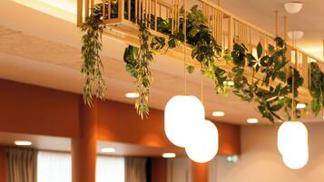 A dining area with wooden tables and chairs, hanging plants, and pendant lights.