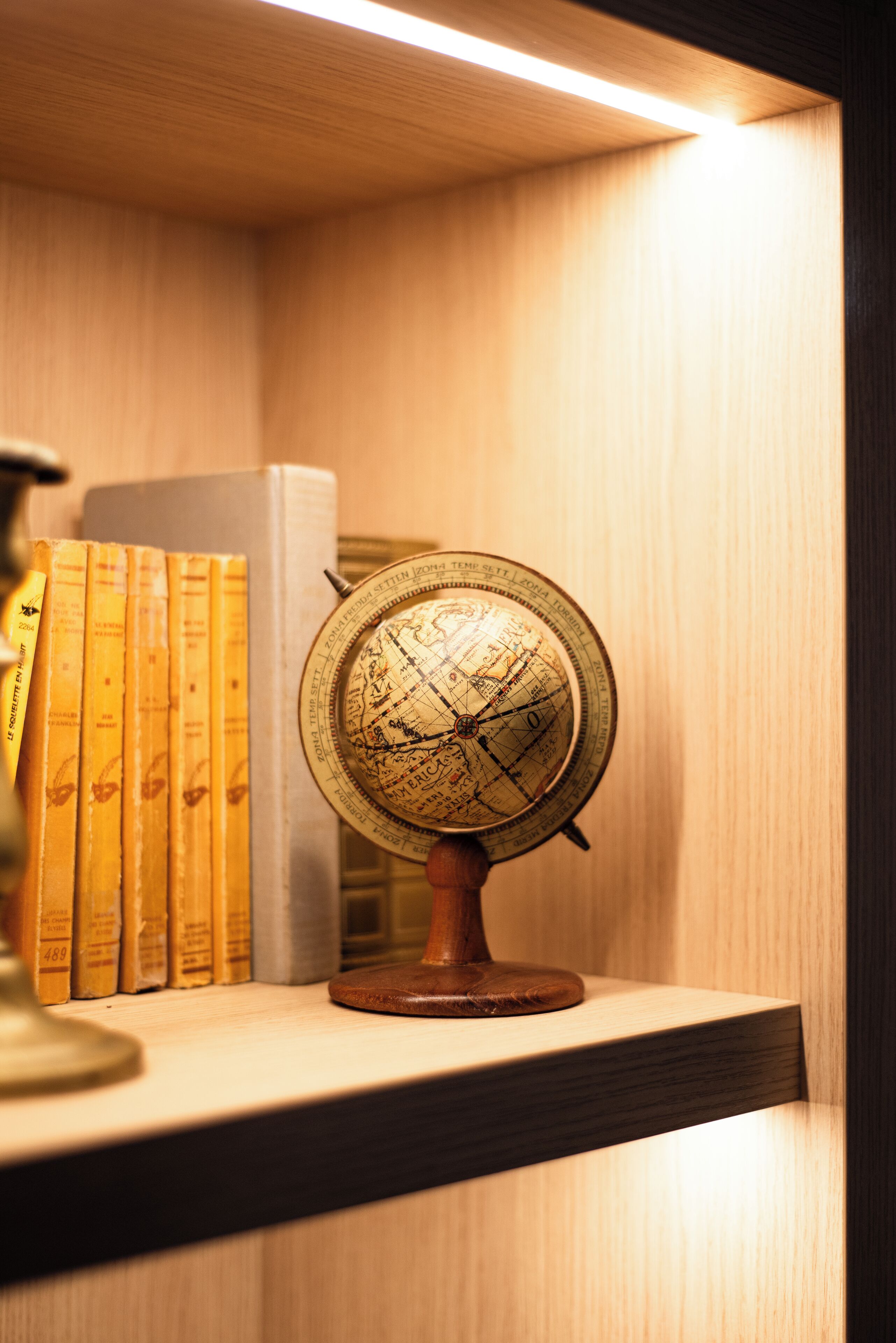 A globe on a wooden stand, surrounded by books on a shelf.