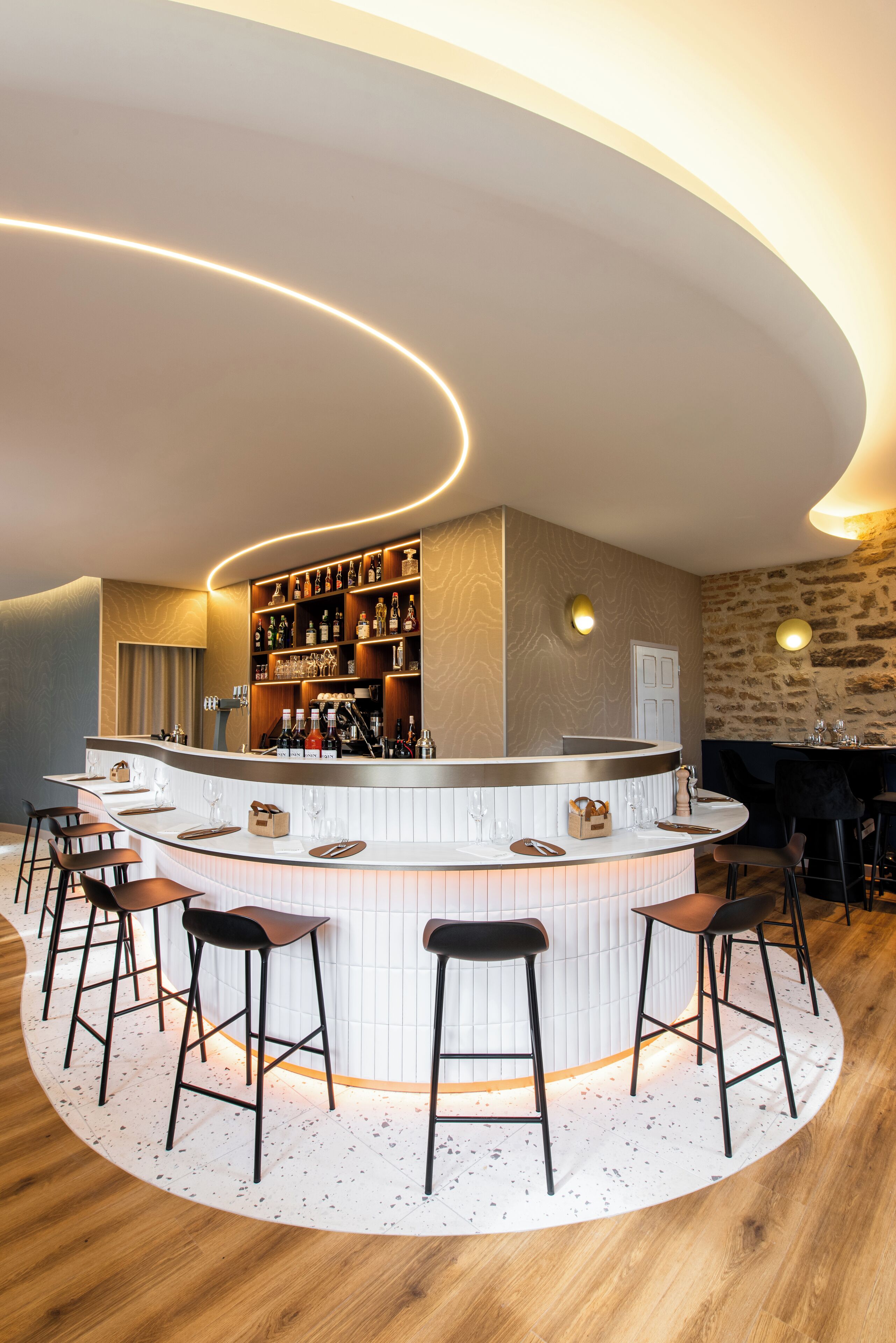 A bar area with a curved counter, stools, and shelves stocked with bottles.