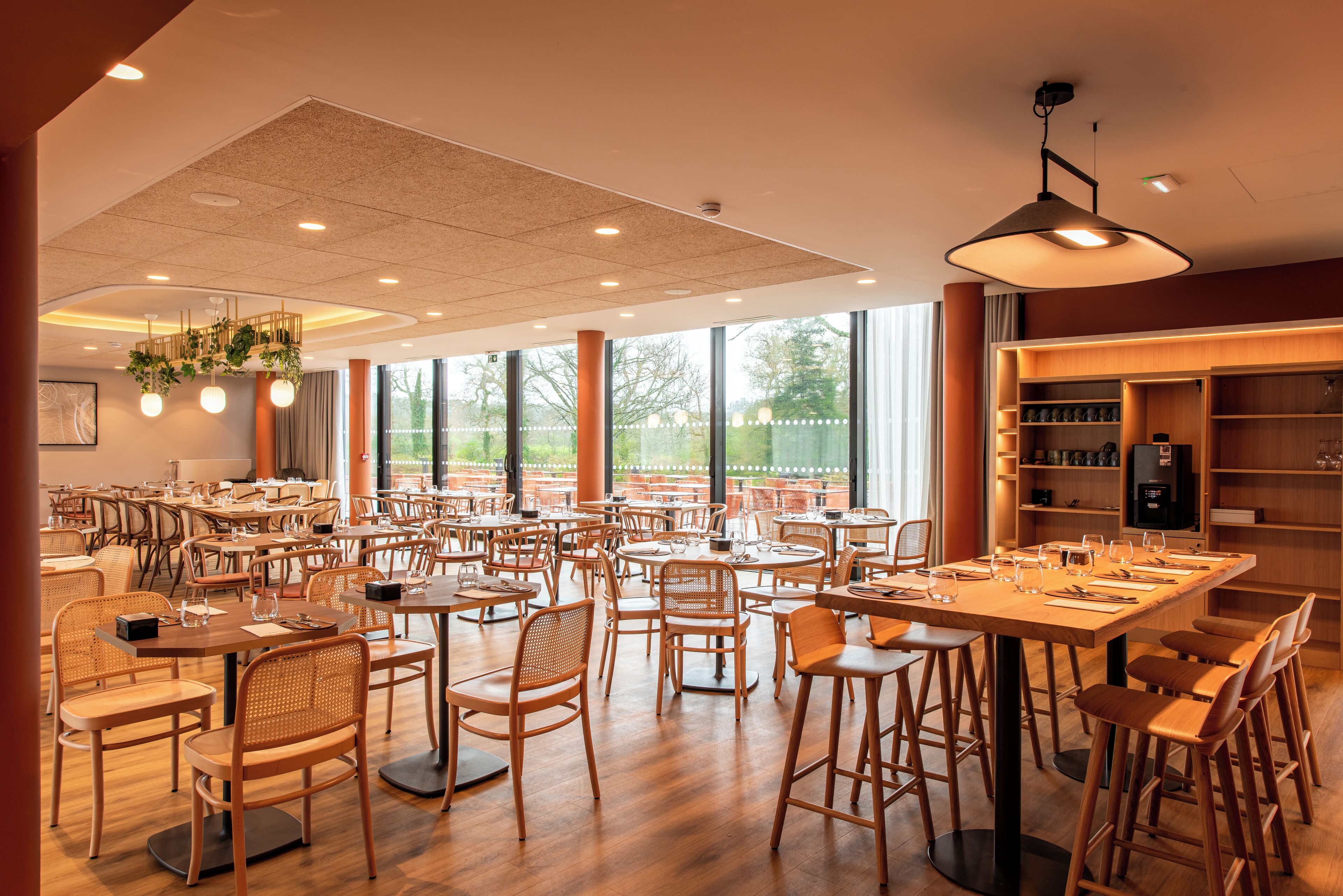A spacious restaurant with multiple tables and chairs, large windows, and a ceiling with recessed lighting.