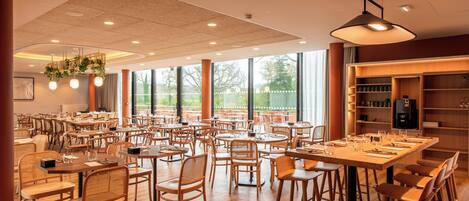 Ein geräumiges Restaurant mit mehreren Tischen und Stühlen, großen Fenstern und einer Decke mit eingelassener Beleuchtung.