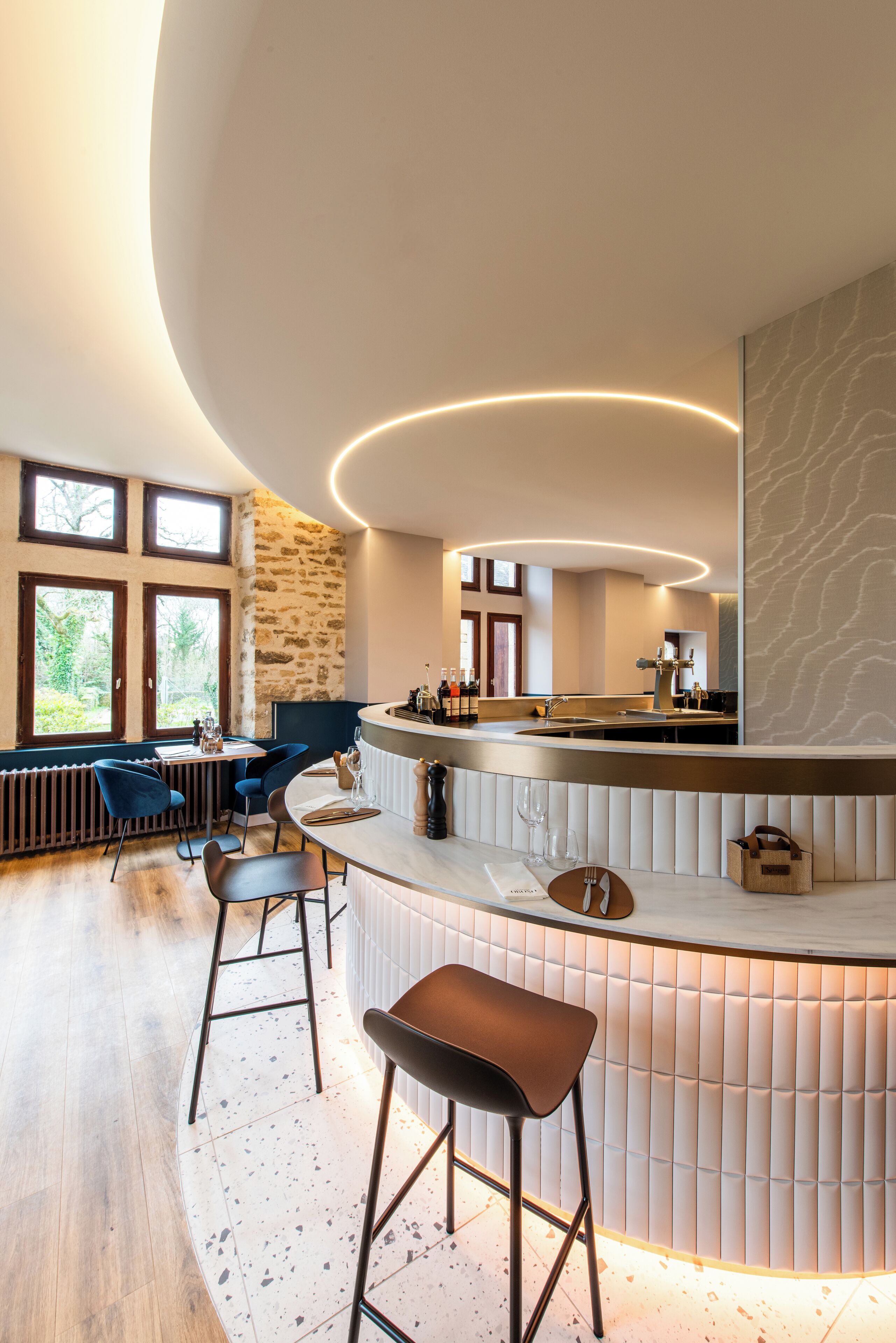 A modern bar area with a curved counter, bar stools, and a stone wall.
