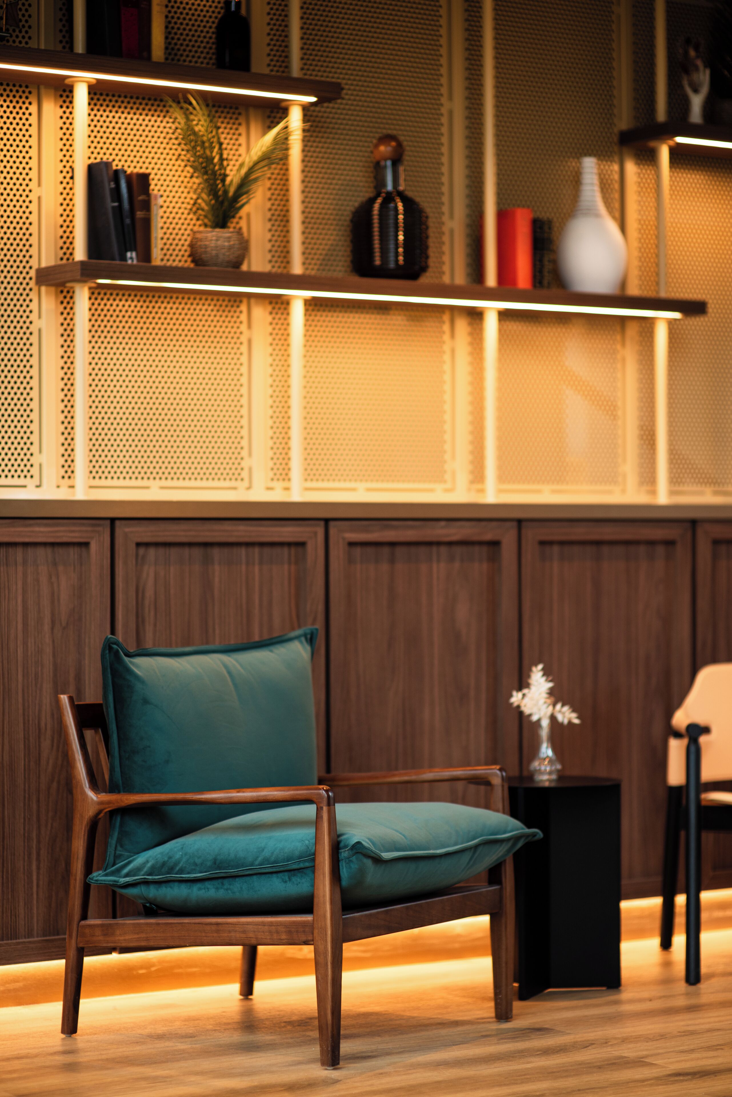 Una silla de madera con un cojín color aguamarina en una habitación con paneles de madera y una estantería con libros y objetos decorativos.