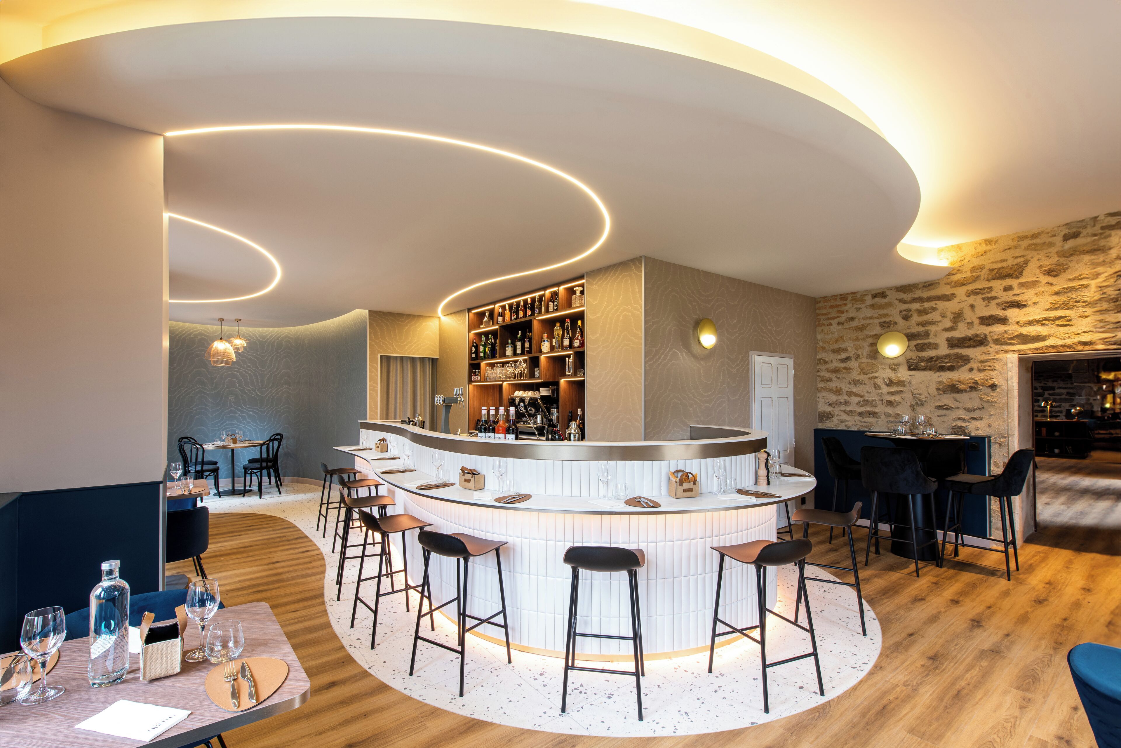 Zona de bar moderna con barra curva, taburetes y una variedad de botellas.