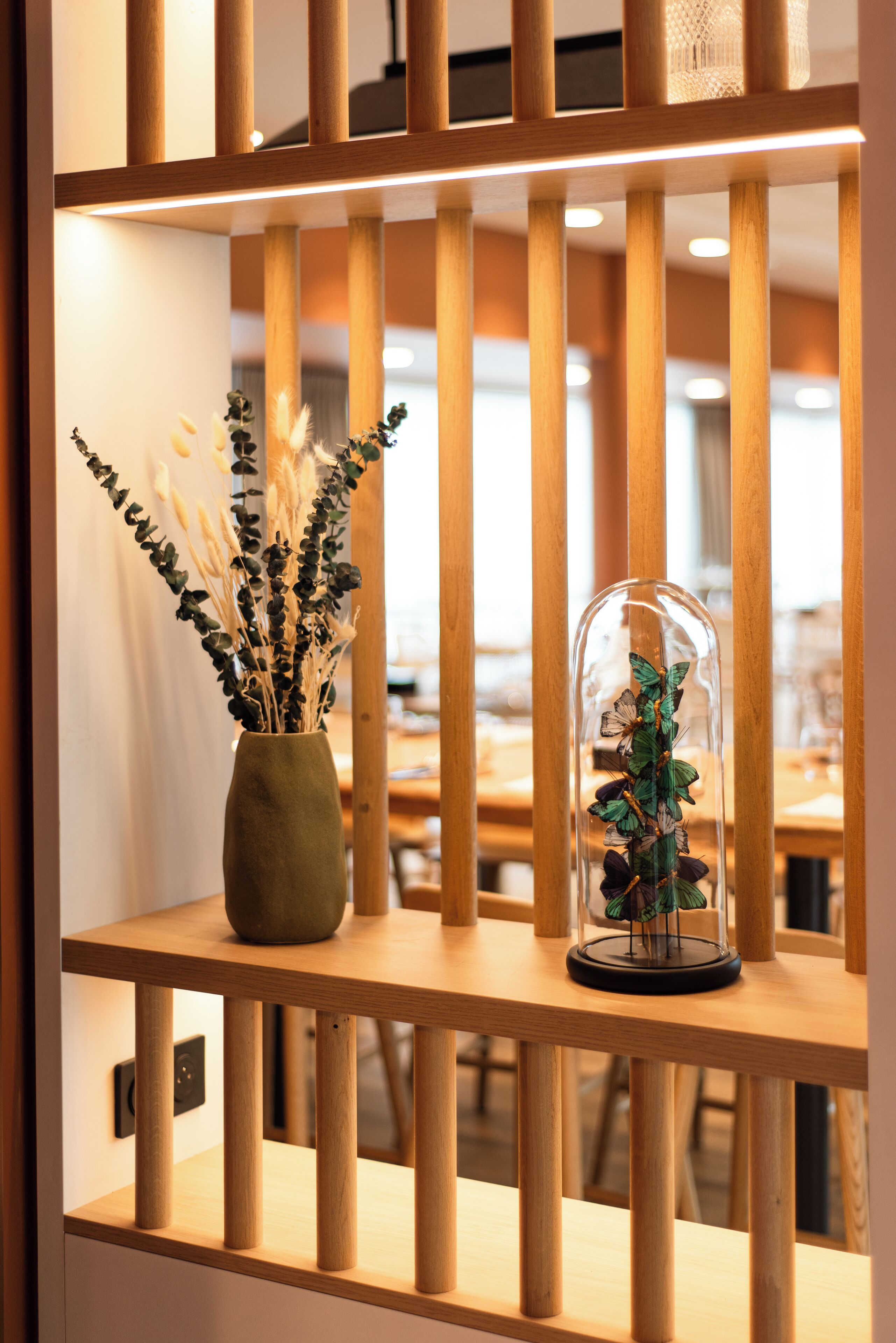 A wooden shelf with a vase of dried plants and a glass dome with butterflies.