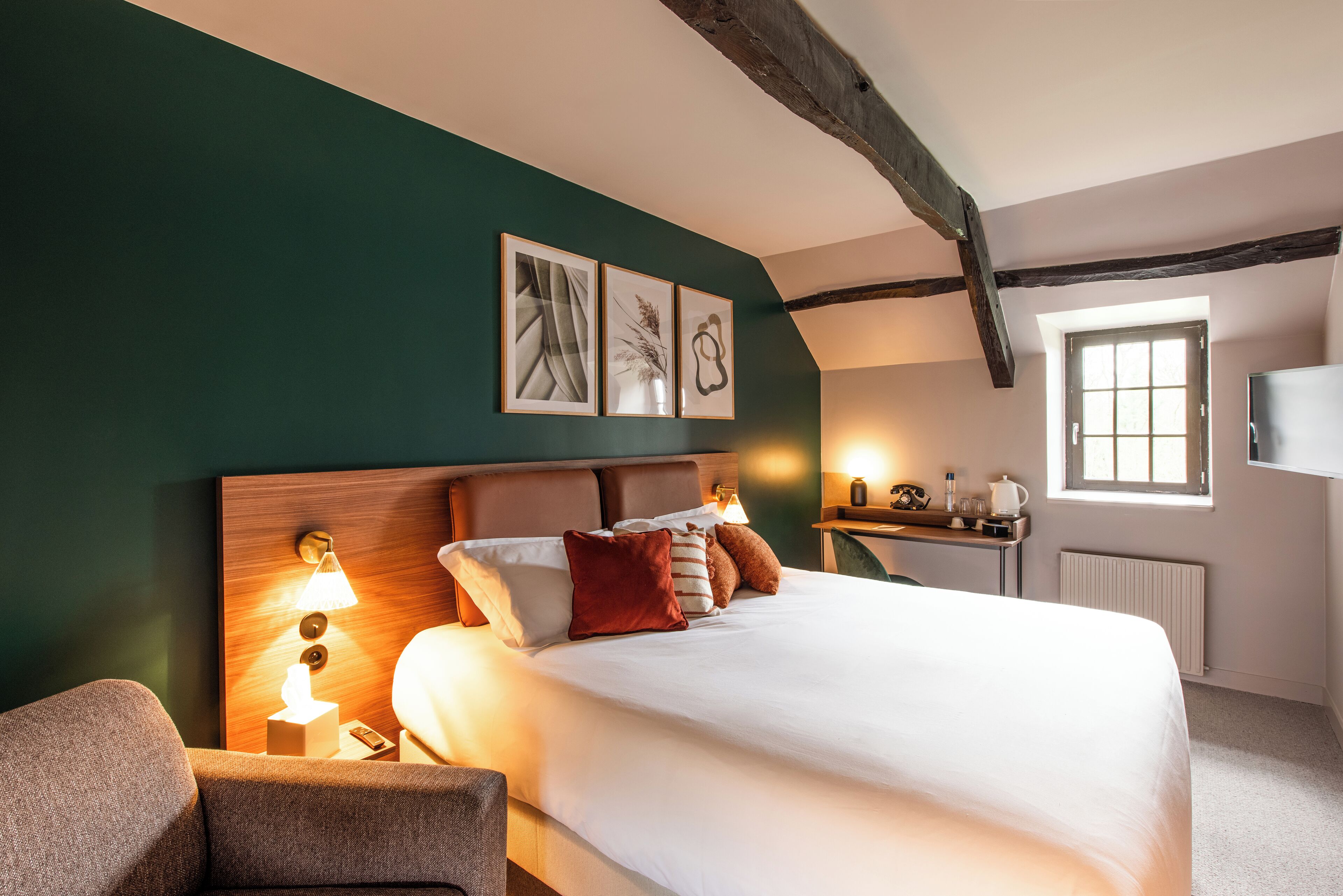 Habitación de hotel con una cama grande, una mesita de noche con lámpara, cabecero de madera y ventana con vistas.