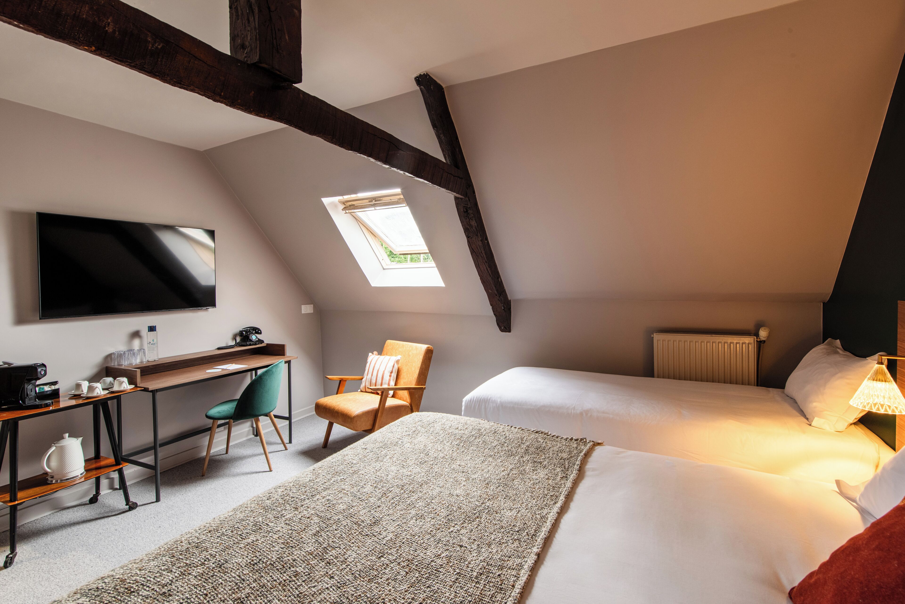 A bedroom with a desk, two beds, a TV, and a skylight.