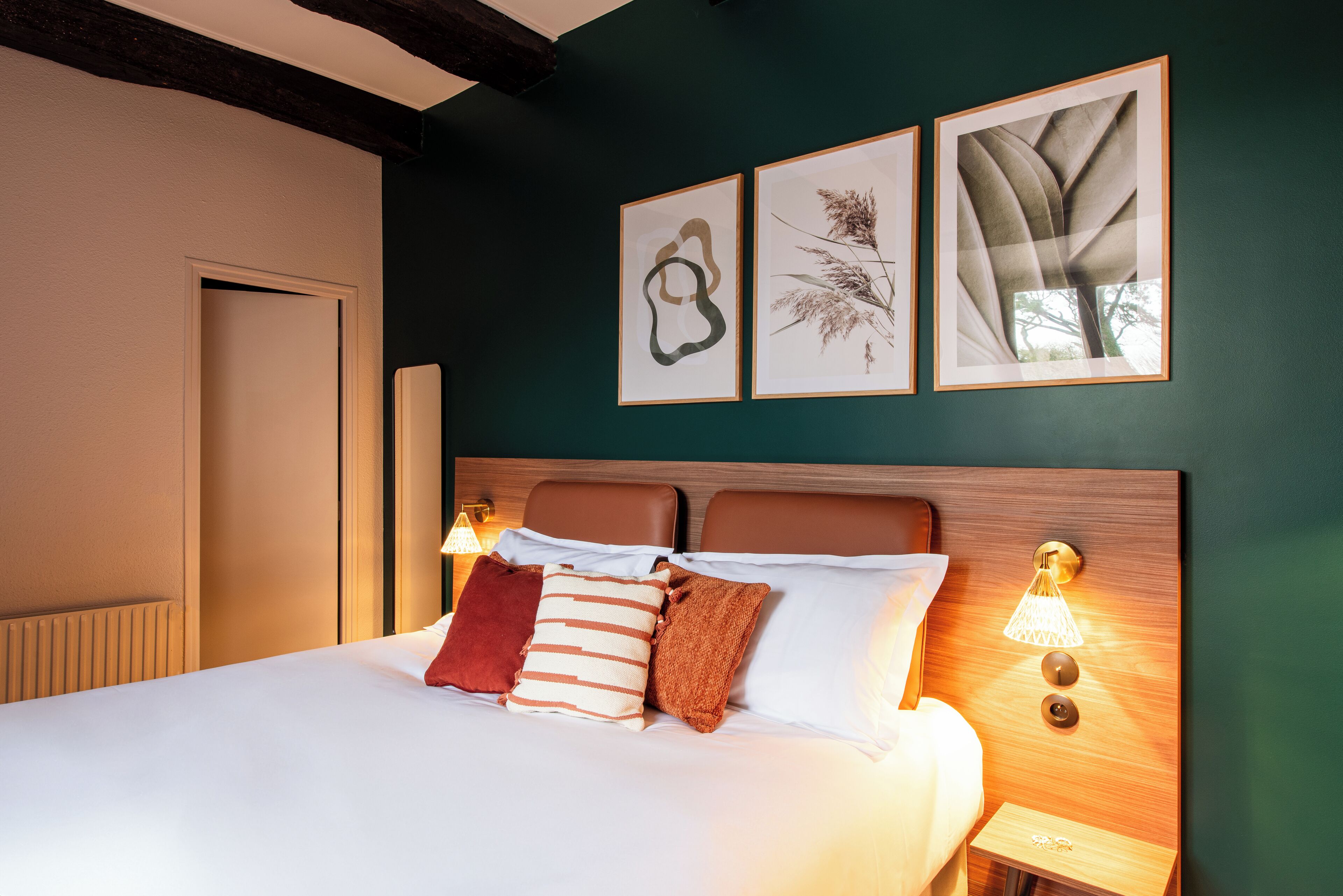 A neatly made bed with multiple pillows, a wooden headboard, and wall-mounted light fixtures.