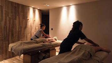 A massage therapy room with two massage tables, wooden paneling on the walls, and recessed ceiling lighting.