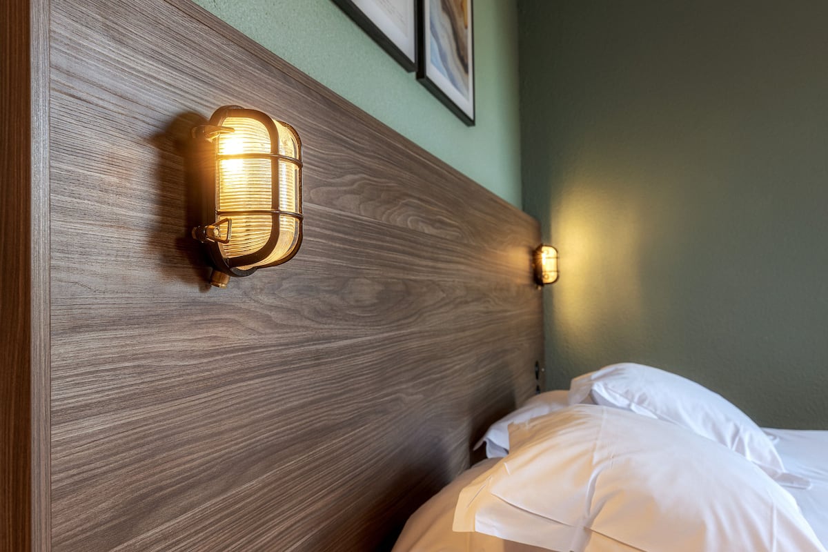 A wooden headboard with wall-mounted light fixtures and a neatly made bed with white linens.