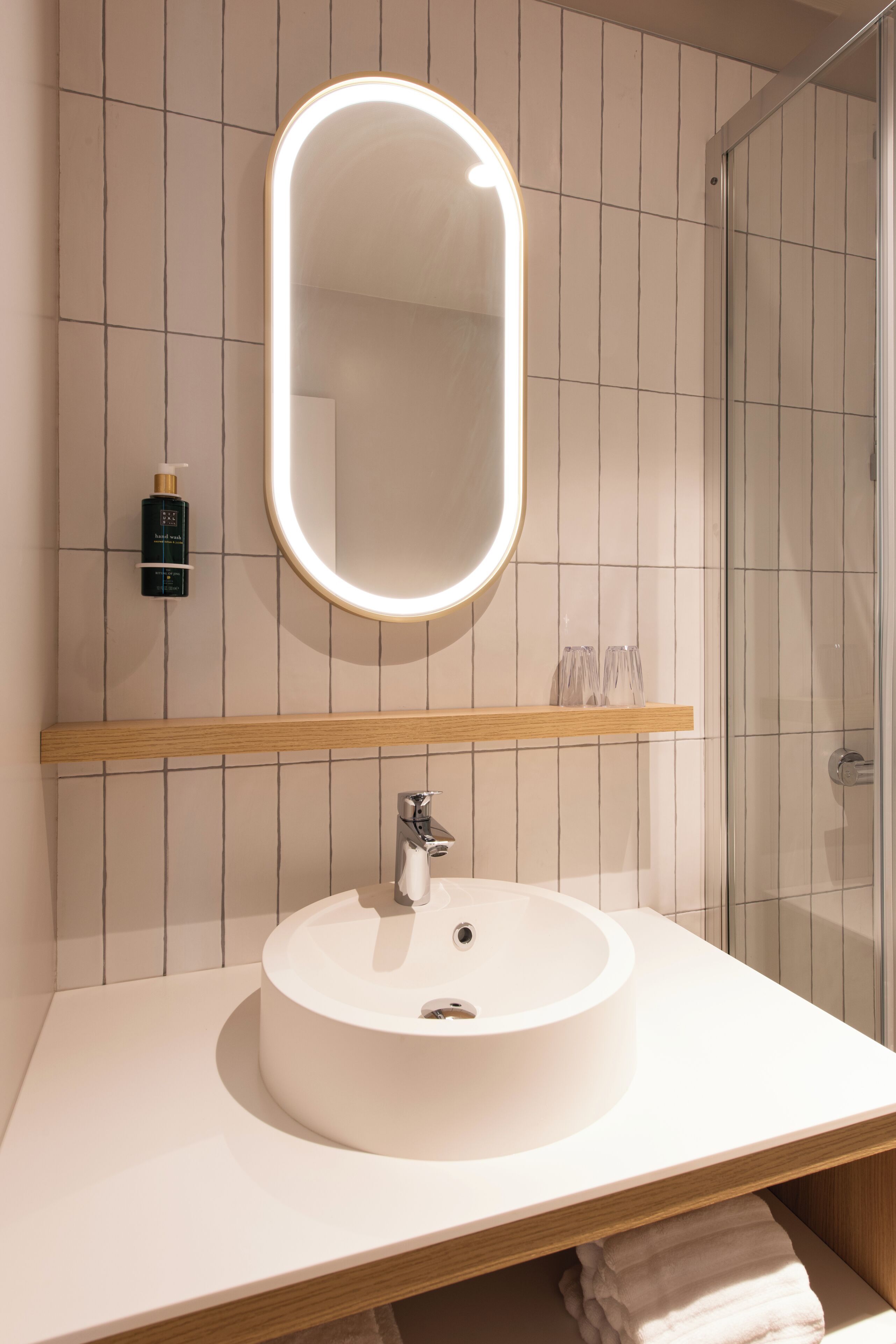 A bathroom with a round sink, a mirror with a light, and a shower area.