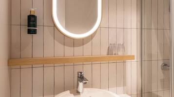 A bathroom with a round sink, a mirror with a light, and a shower area.