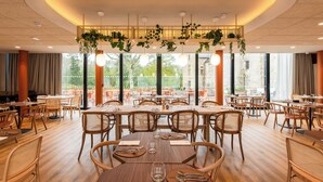 Un comedor amplio con varias mesas y sillas, ventanas grandes y plantas colgantes.