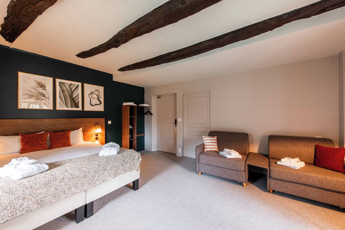 A hotel room with a bed, two sofas, a bookshelf, and artwork on the wall.