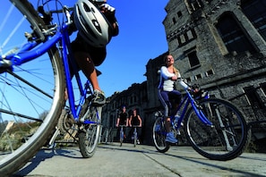 Cyclists ride along a scenic path past a historic building with classic architecture.