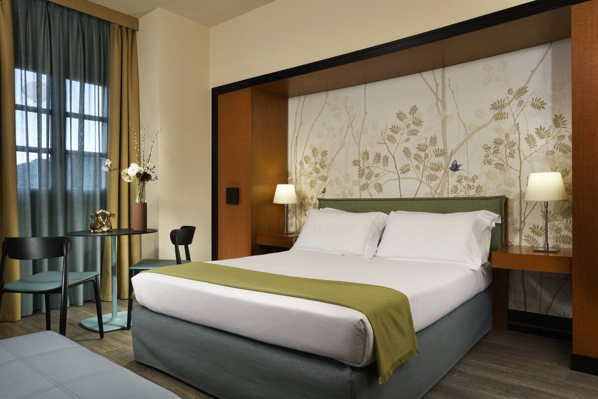 Una habitación de hotel con una cama grande, dos sillas, una mesita y un panel decorativo en la pared.