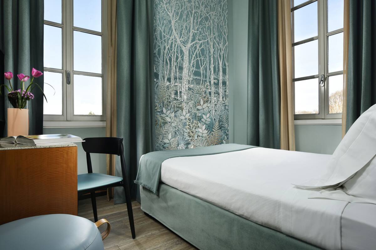 Un dormitorio con cama, escritorio, silla y ventana con cortinas.