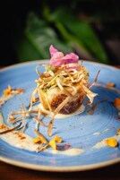 Un dessert su un piatto blu, decorato con elementi essiccati e un fiore rosa.