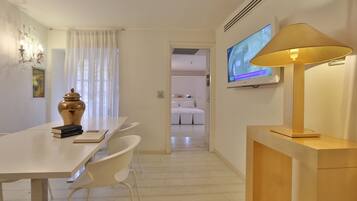 Una habitación de hotel con comedor, televisor montado en la pared y una lámpara.