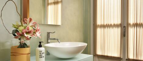 A bathroom with a white sink, a mirror, and a vase with flowers.
