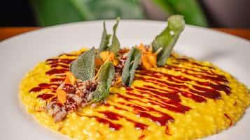 Un piatto di cibo con una base gialla, guarnito con foglie verdi e salsa rossa.