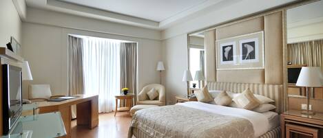 A hotel room with a large bed, a desk, a chair, a TV, and a mirror.