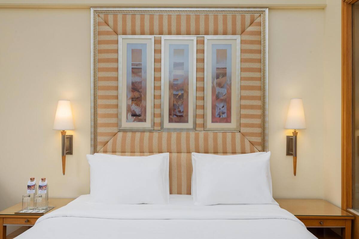 Ein Hotelzimmer mit einem großen Bett, zwei Nachttischen mit Lampen und einem dekorativen Kopfteil mit gerahmten Kunstwerken.