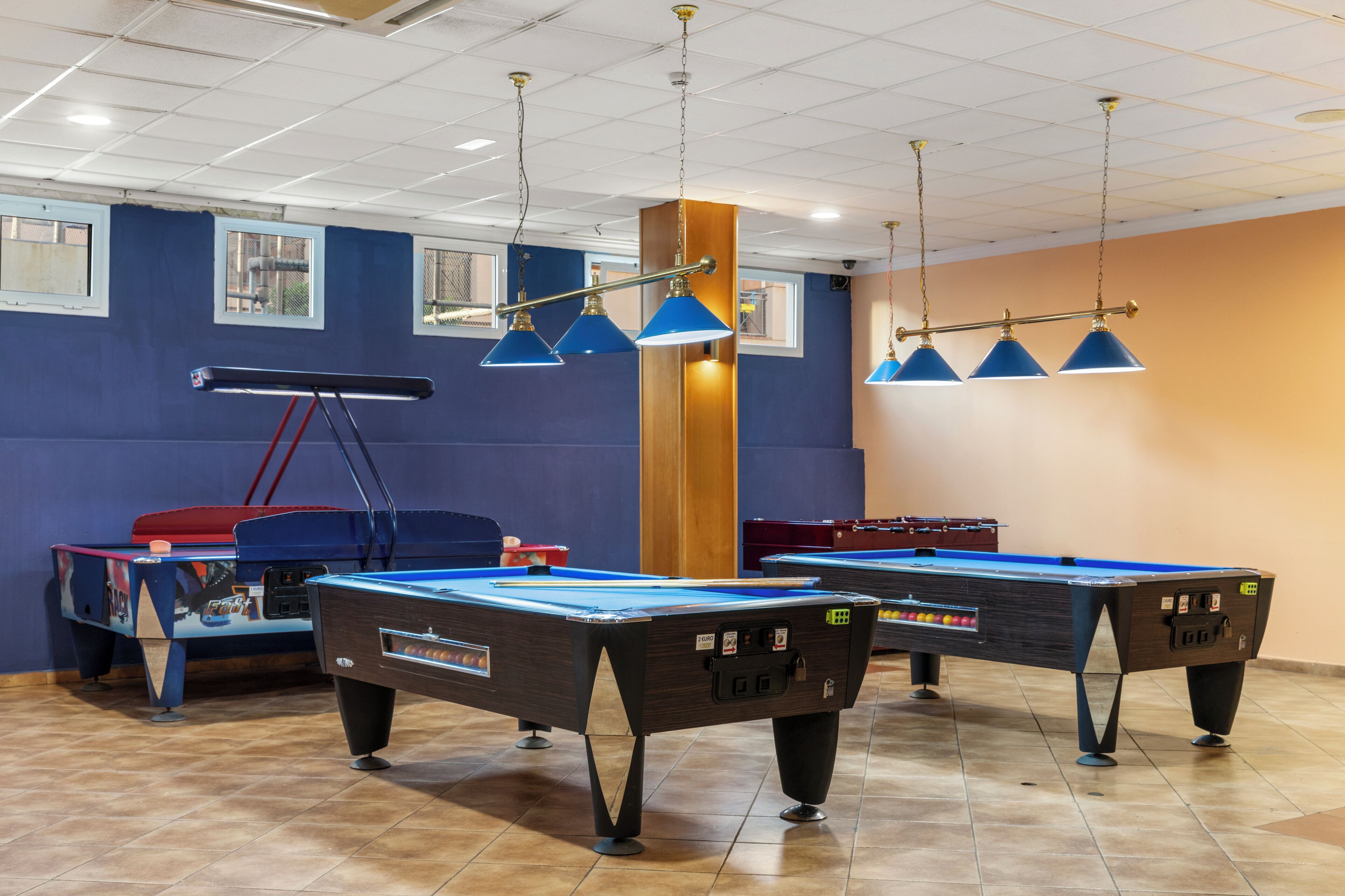A pool table area with multiple tables, overhead lighting, and a tiled floor.