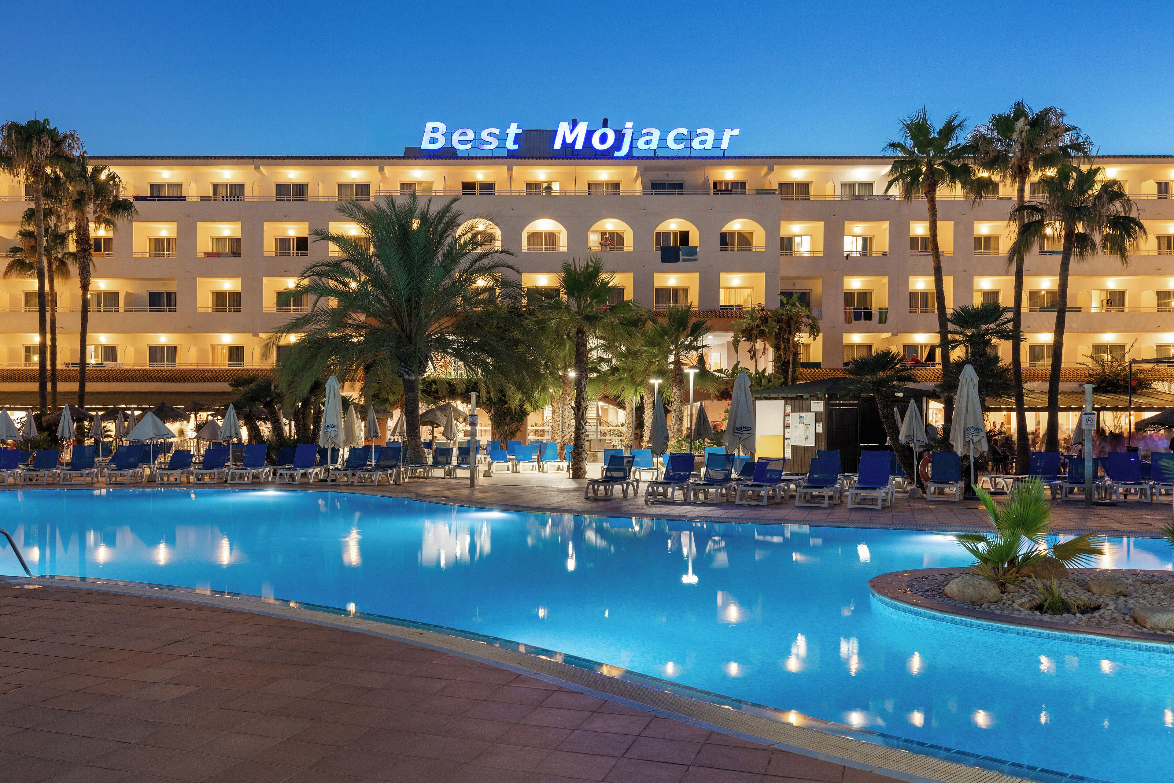 A hotel with a swimming pool, palm trees, and lounge chairs.
