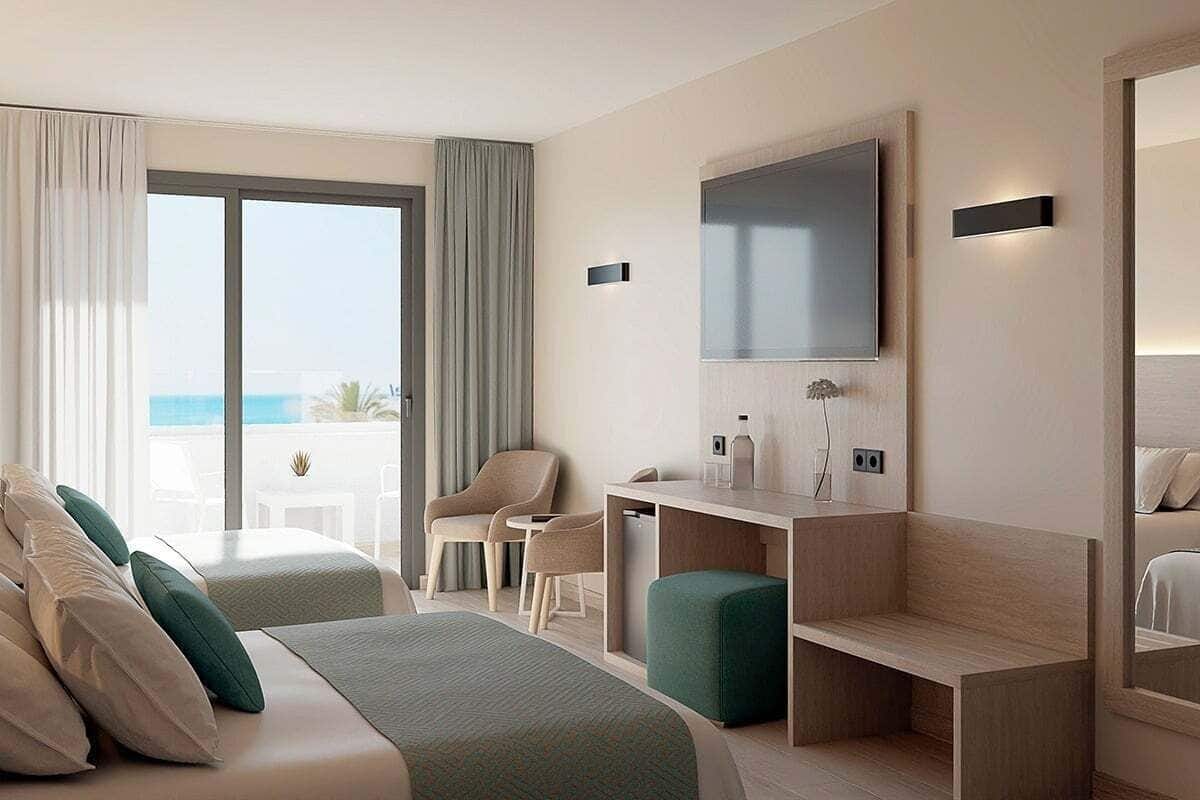 A hotel room with two beds, a desk, a chair, a TV, and a balcony with a view of the sea.