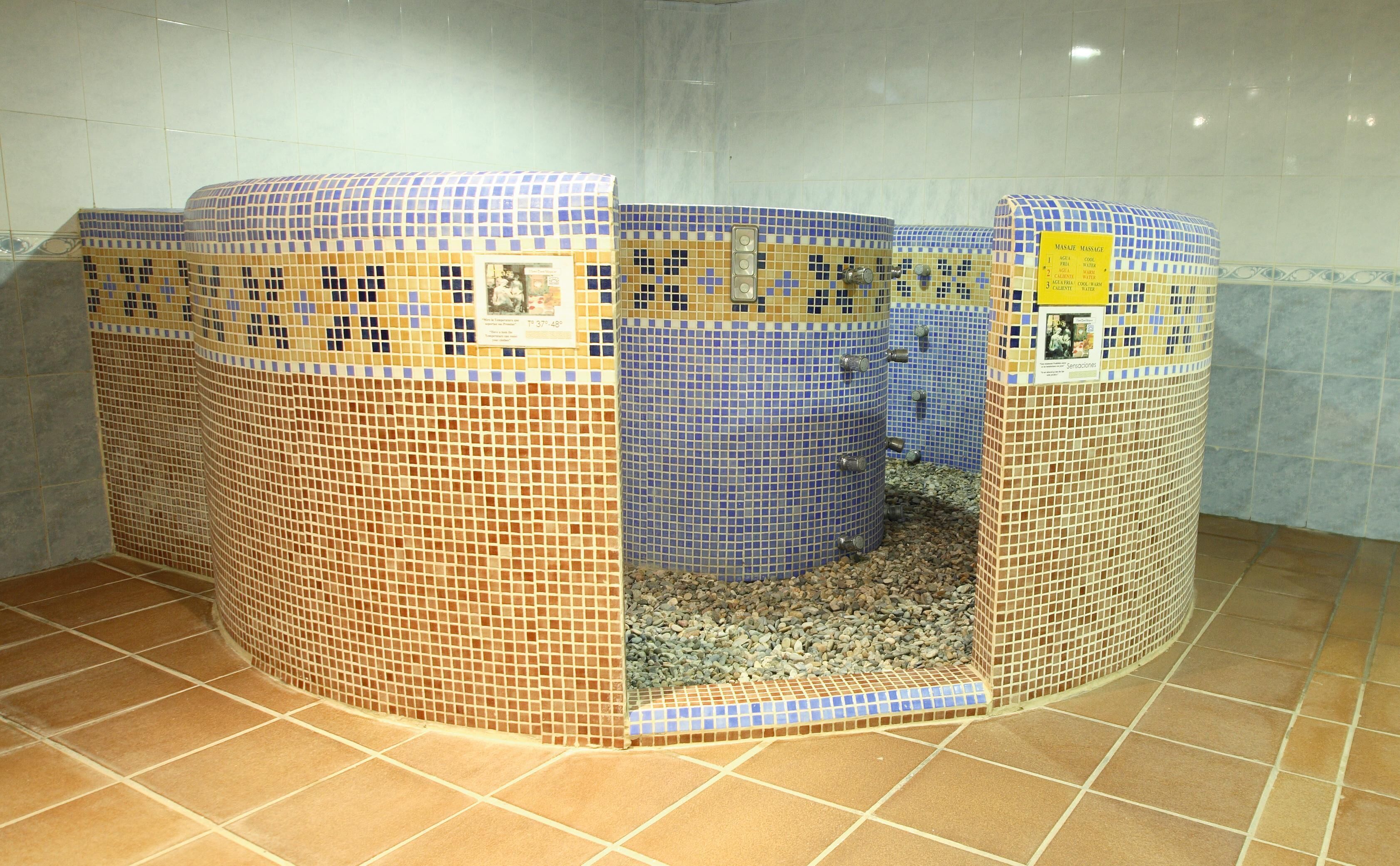 A bathroom with a mosaic-tiled shower enclosure, a tiled floor, and a yellow sign indicating a massage service.