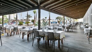 An outdoor dining area with tables and chairs, a wooden ceiling, and a view of palm trees and buildings. - Hotel Best Mojácar (Mojacar)