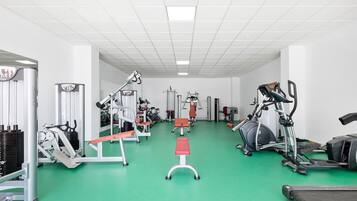 Ein Fitnessraum mit unterschiedlichen Trainingsgeräten, einem grünen Boden und weißen Wänden.