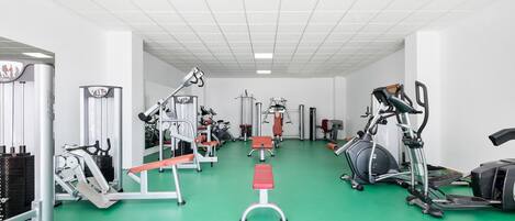 Un gimnasio con equipo de ejercicio diverso, suelo verde y paredes blancas.