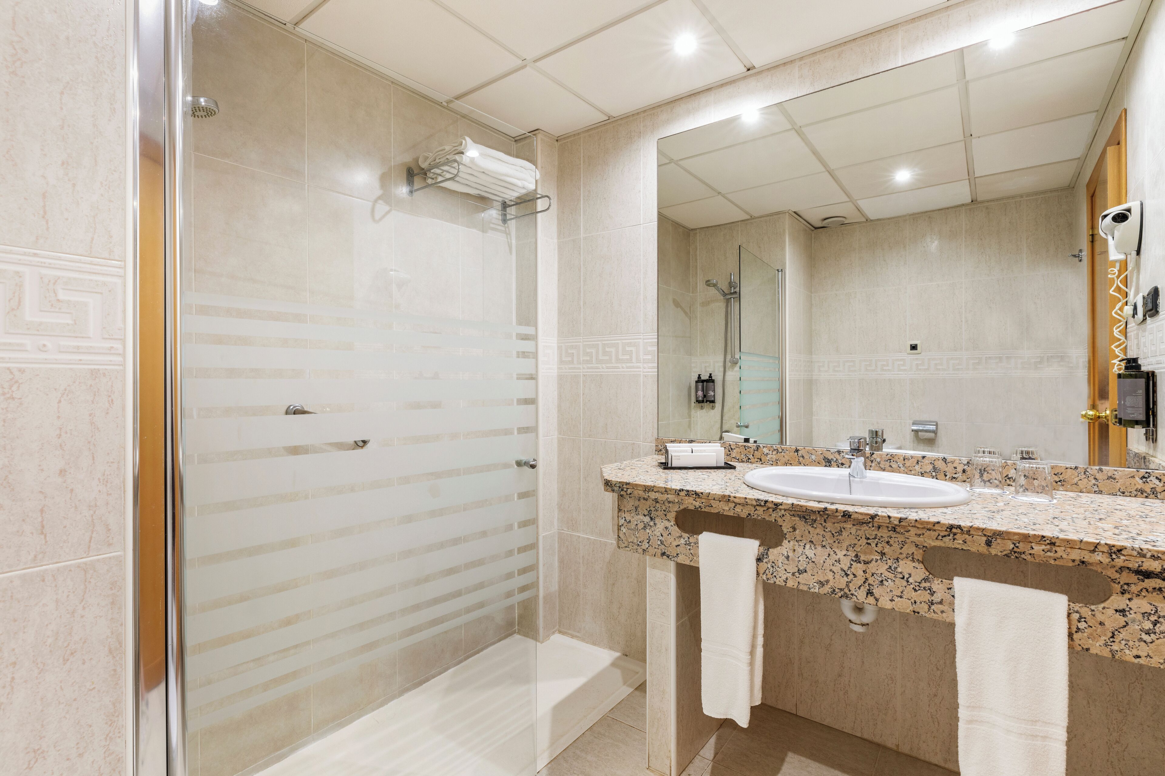 A modern bathroom with a glass-enclosed shower, a marble vanity with a sink, and a large mirror.