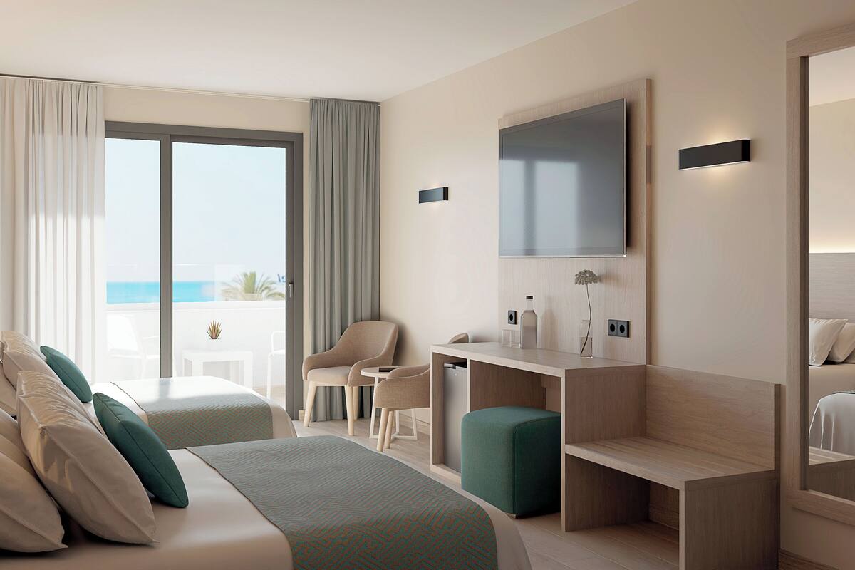 A hotel room with a bed, two chairs, a desk, a TV, and a view of the sea.