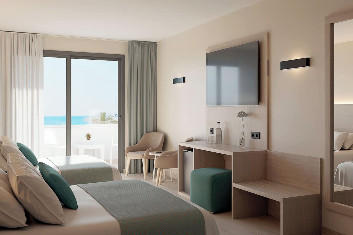 Habitación de hotel con cama, dos sillones, un escritorio, un televisor y vistas al mar.