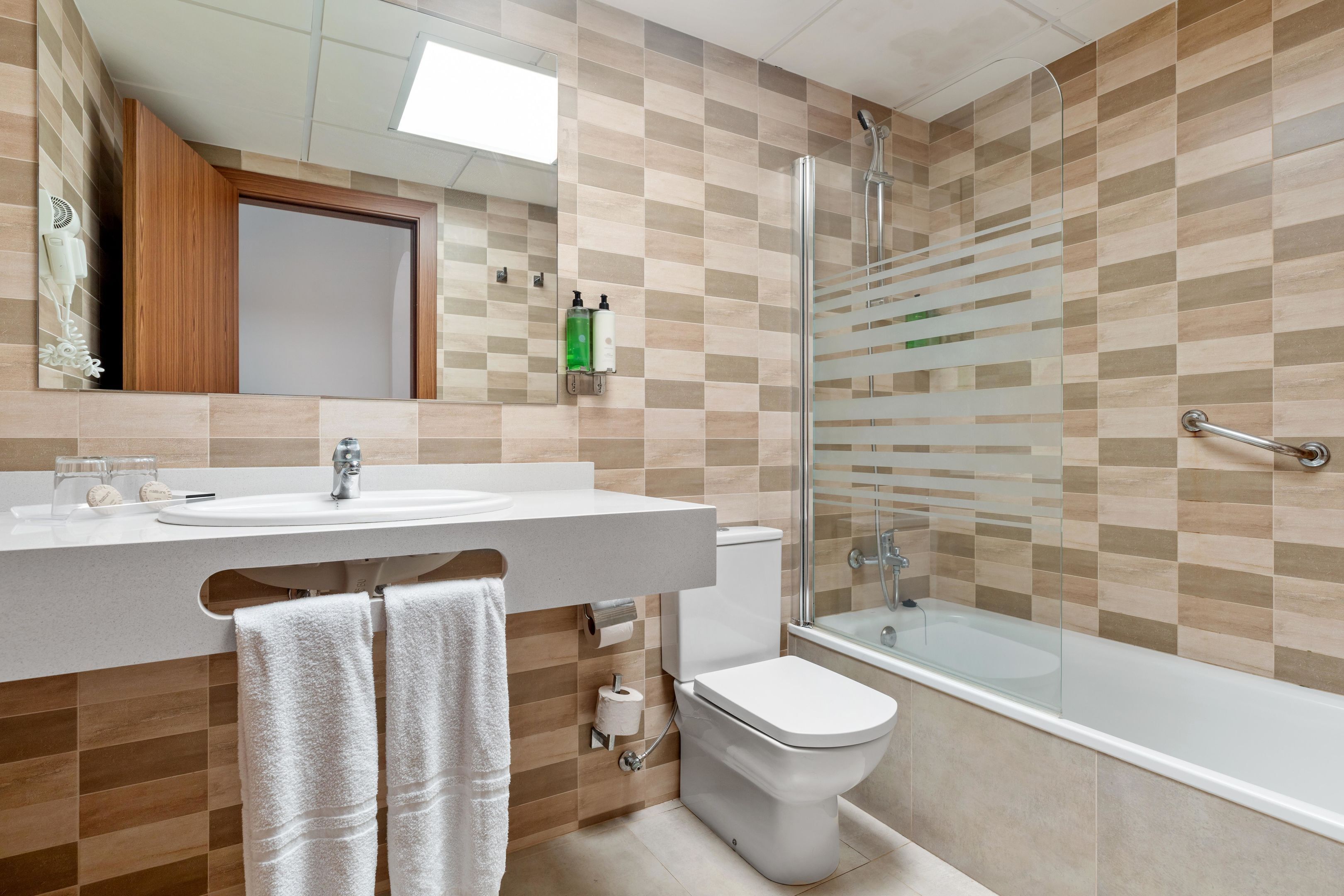 Un baño moderno con lavamanos, inodoro y ducha con mampara de vidrio.