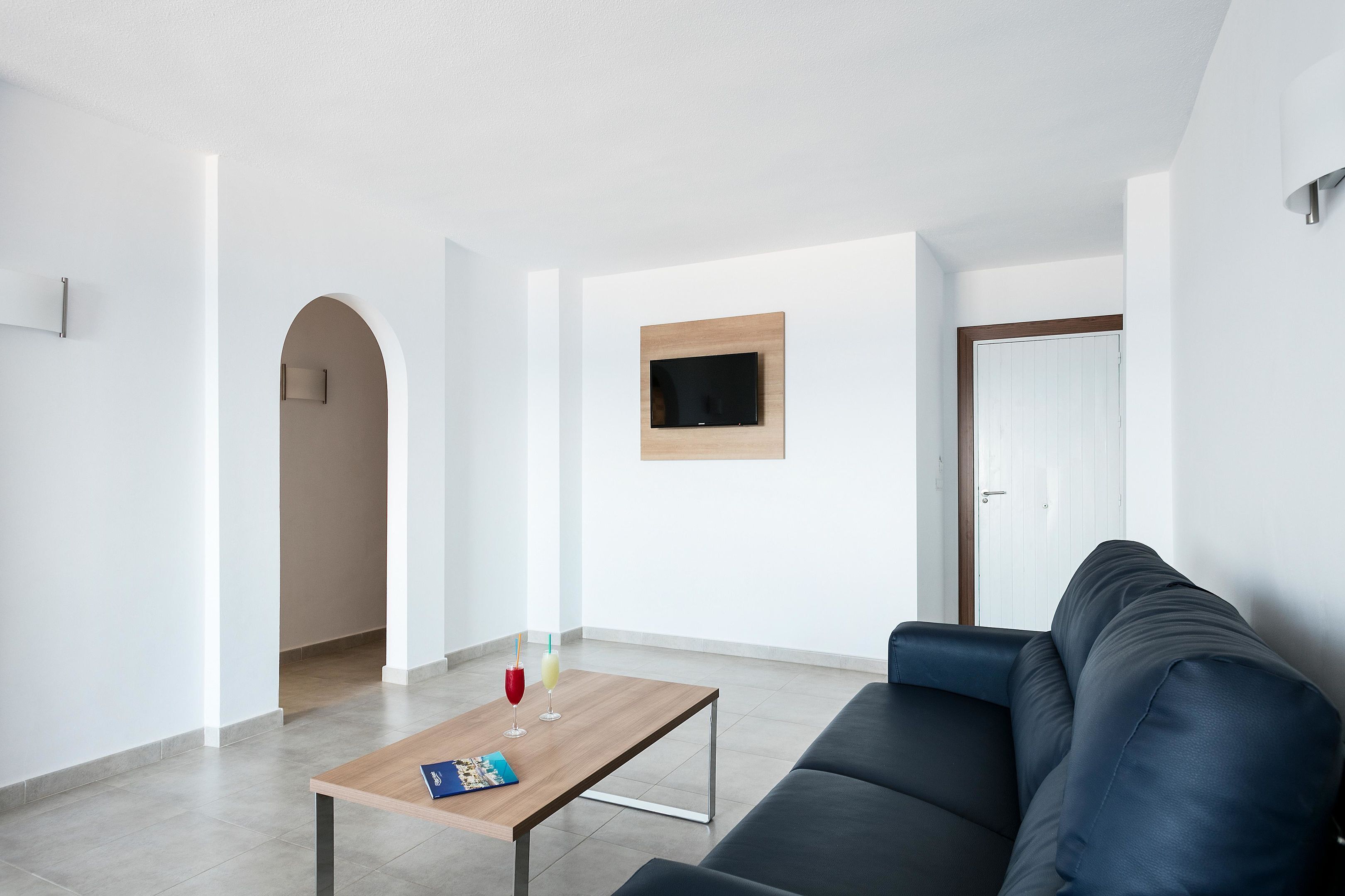 A modern living room with a dark blue sofa, a wooden coffee table with a magazine, and a TV mounted on the wall.